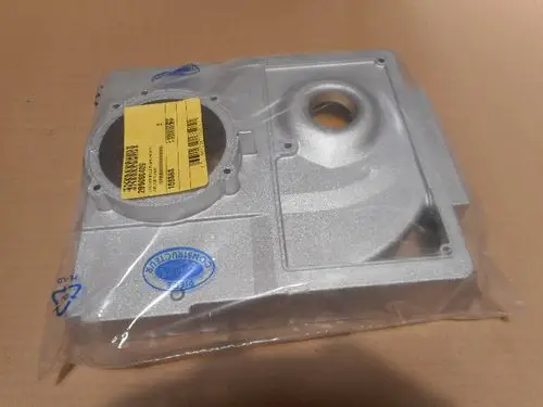 Remeha Brennergehäuse in transparentem Schutzbeutel, deutlich strukturiert mit einem runden Element und mehreren Anschlüssen, auf braunem Kartonuntergrund.